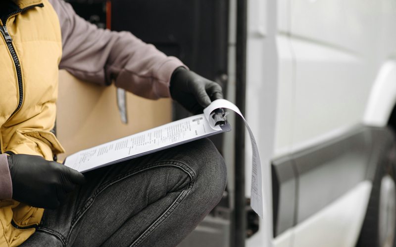 Driver with shipping documents by a delivery van — road transport